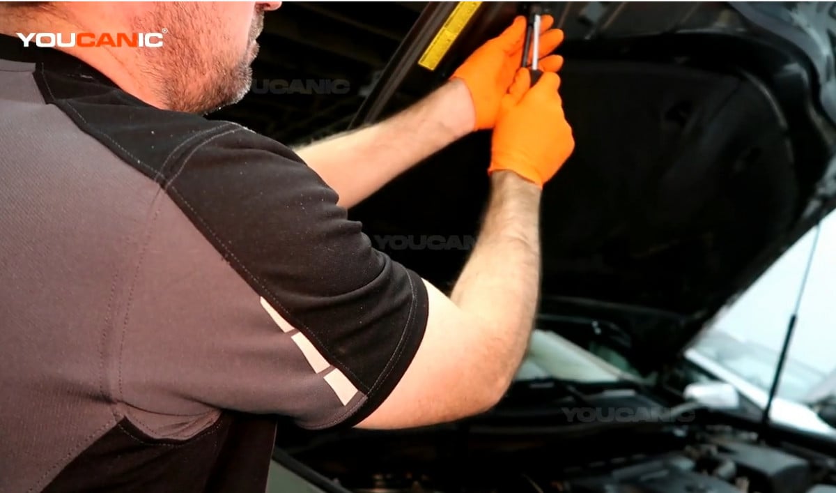 Inserting the flat screwdriver into the tab holding the hood strut.