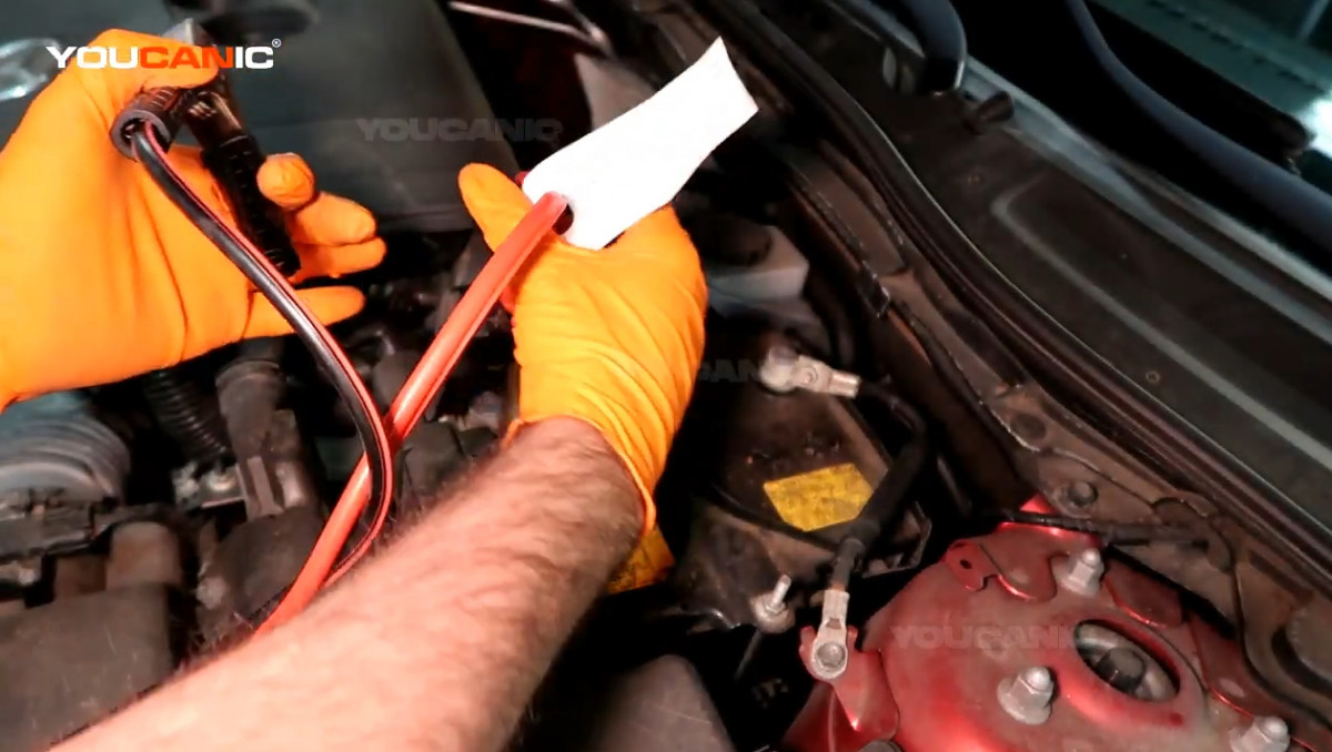 Connecting the red jumper cable to the positive terminal of the battery.